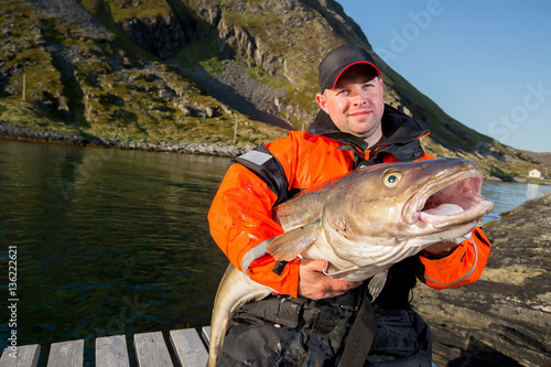 male fisherman holding a huge fish Cod