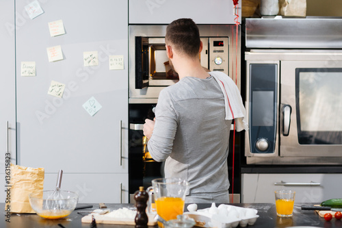 Young man putting container with food into microwave oven