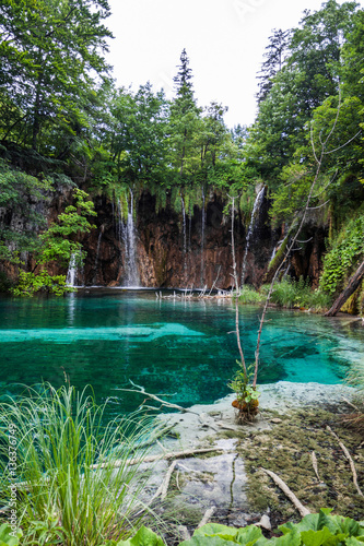 Forest waterfall falls into a turquoise, crystal-clear lake. Pli