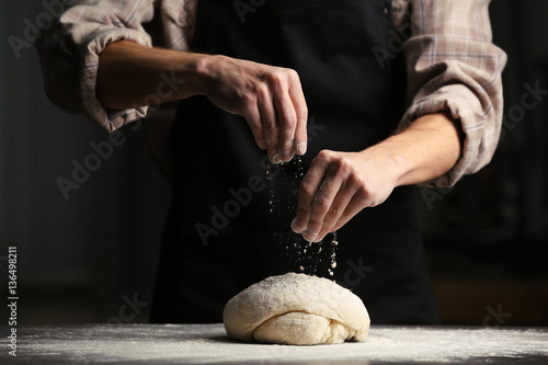 Man sprinkling flour over fresh dough on kitchen table