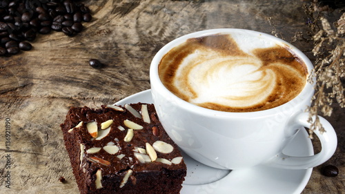Cappuccino Coffee and sweet chocolate brownies cake. A cup of latte, cappuccino or espresso coffee with milk put on a wood table with dark roasting coffee beans. Drawing the foam milk on top.