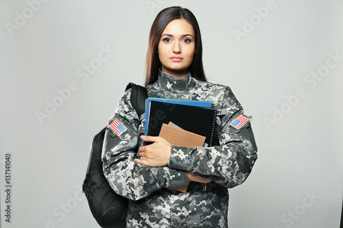 Pretty female cadet of military school on grey background