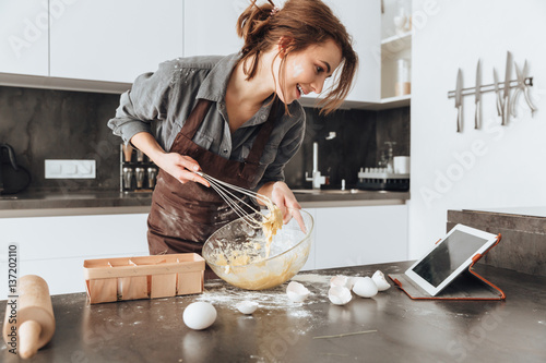 Cheerful woman cooking and looking at tablet computer.