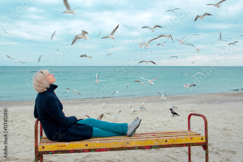 blonde woman and seagulls in cloudy autumn day on the sea coast 