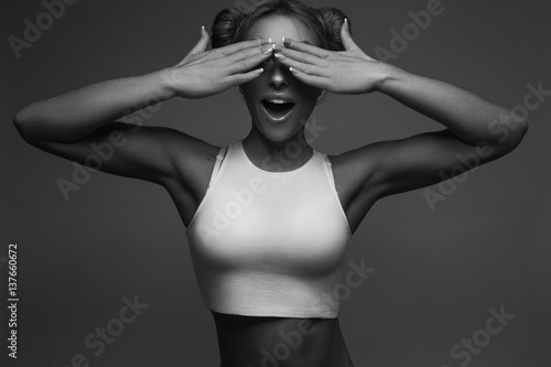 Спортивная девушка закрывает глаза руками и удивленно улыбается (черно-белая фотография) 