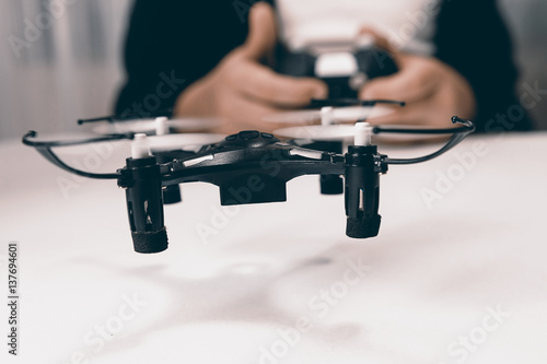 Boy hands with a remote control flying a small drone toy indoors.