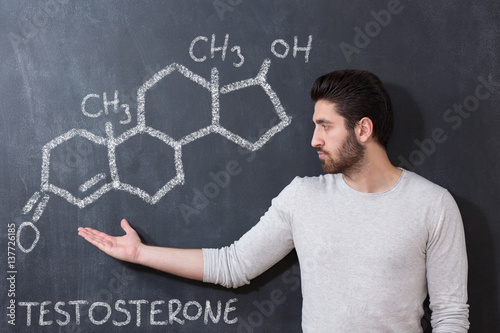 chemical structure of testosterone molecule drawn on chalkboard background with man in front of it