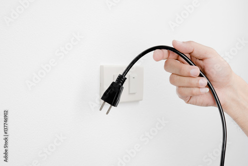 Hand of man unplug electric outlet plug on wall white background safety concept