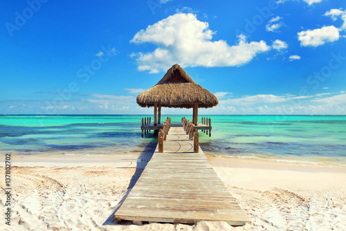 Tropical white sandy beach. Palm leaf roofed wooden pier with gazebo on the beach. Cross processed. Instagram filter. Punta Cana, Dominican Republic