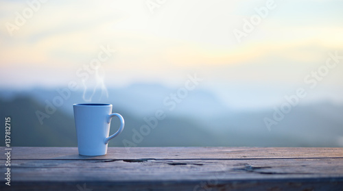 Cup with coffee on table over mountains landscape with sunlight. Beauty nature background..