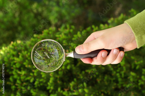 Magnifying glass in hand against plant