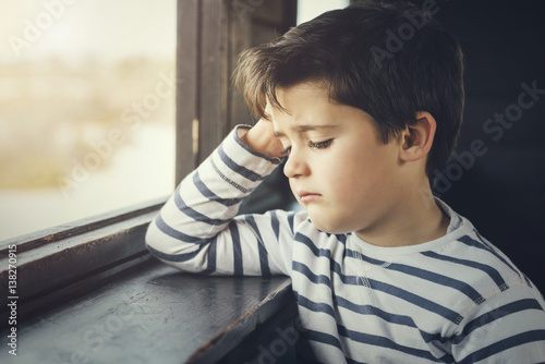 niño triste al lado de una ventana