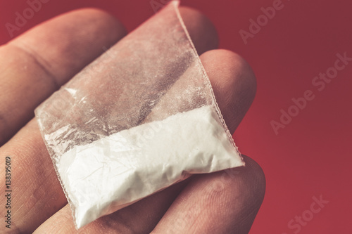 Mans hand holding or giving, selling on palm plastic packet with cocaine powder 