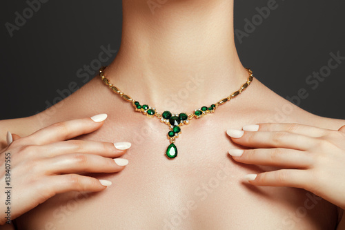 Elegant fashionable woman with jewelry. Beautiful woman with a emerald necklace. Beauty young model with a diamond pendant on a gray background. Jewellery and accessories.