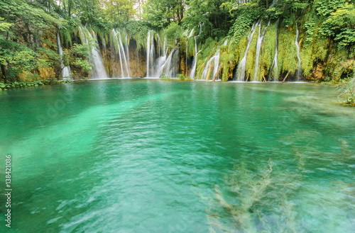 Multiple stunning waterfalls cascade into a vibrant turquoise lake at one of the oldest and most visited national parks in Europe, Plitvice Lakes National Park.