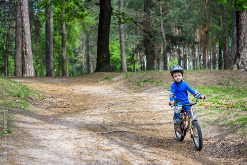 Happy cute blond kid boy having fun his first bike on sunny summer day, outdoors. child making sports. Active leisure for children. wear safety helmet. is smiling and cicling