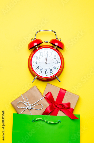 cute gifts in beautiful green shopping bag and alarm clock on wonderful yellow background