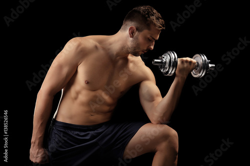 Sporty man doing exercises with dumbbell on black background