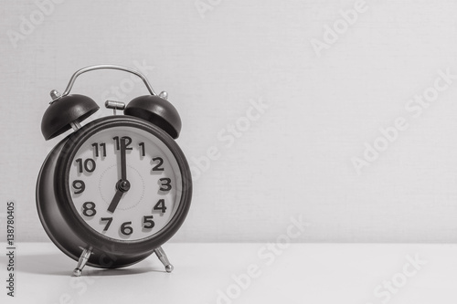 Closeup alarm clock for decorate in 7 o'clock on white wood desk and cream wallpaper textured background in black and white tone with copy space