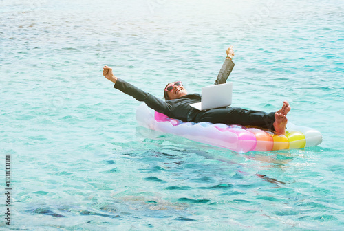 Happy businesswoman resting on lilo with laptop