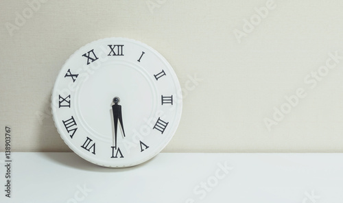 Closeup white clock for decorate show half past five p.m. or 5:30 p.m. on white wood desk and cream wallpaper textured background with copy space