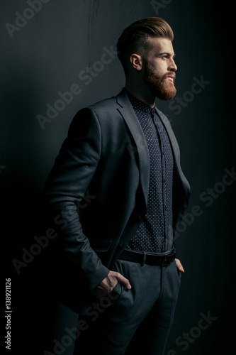 Stylish handsome bearded man in trendy suit looking away on black