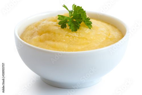 Cooked cornmeal polenta with green parsley in white ceramic bowl isolated on white.
