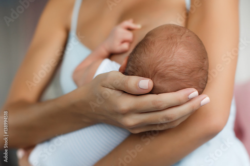 Happy young mother, sitting in the bedroom with her newborn son in her arms,gently supports the child's head with your hand, feeds the baby's chest,the boy greedily sucks her mother's breast