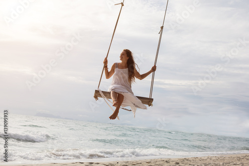 Beautiful young female sitting on the swing on sea shore enjoy summer