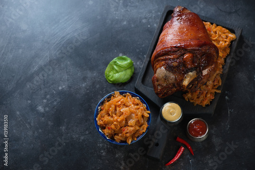 Whole baked pork knuckle and braised cabbage on a scratched metal surface, high angle view with copyspace