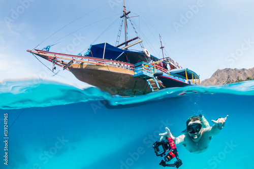 A freediver swims underwater next to a traditional boat on a tropical coral reef