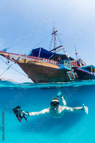 Snorkeller freedives below the surface in front of a traditional wooden boat