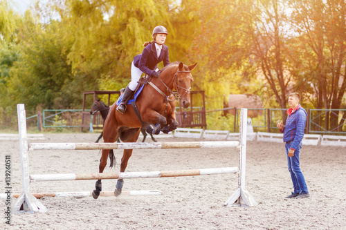 Young horseback sportswoman jumping over obstacles on show jumping training with trainer