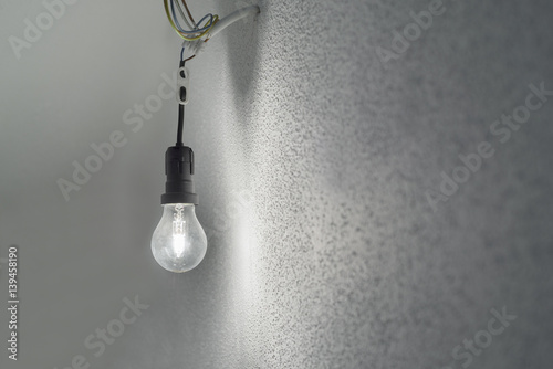 Halogenglühlampe in einer schwarzen Kunststoff-Fassung mit Lüsterklemme aus an einer Wand mit weissem Rauhputz herausragenden Stromkabeln