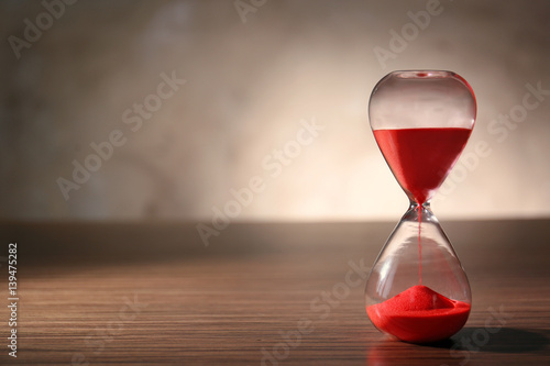 Crystal hourglass with red sand on wooden table