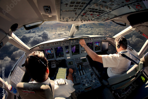 Flight Deck of modern passenger jet aircraft. Pilots at work. Cloudy sky and sunset view from the airplane cockpit.