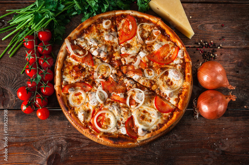 Traditional italian food. Delicious fresh pizza with tomatoes, chicken and onion on wooden background with ingredients, flat lay.