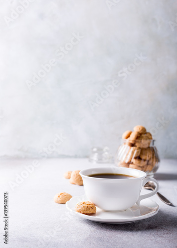 White cup of coffee with amaretti cookies on light gray background with copy space.