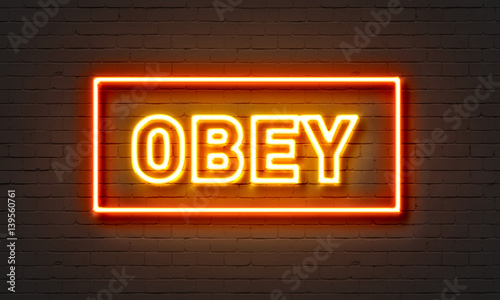 Obey neon sign on brick wall background.