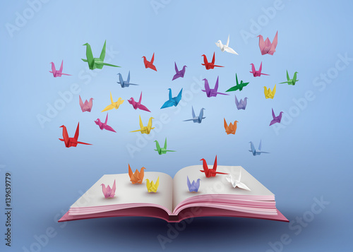 origami made colorful paper bird flying over open book