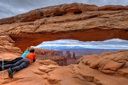 Friends enjoying the view of canyon and mountains. Mesa Arch. Canyonlands National Park. Moab. Utah. United States.