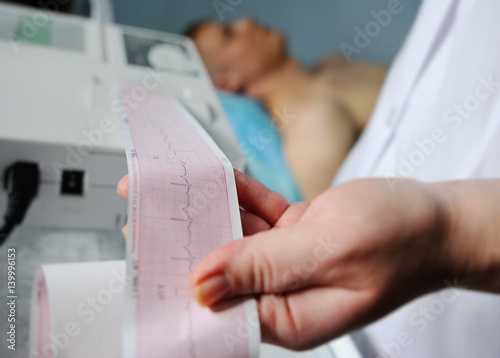 doctor with electrocardiogram equipment making cardiogram test to male patient in hospital clinic