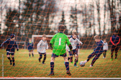 Young soccer goalie defending the net with forward player striking the ball in the background