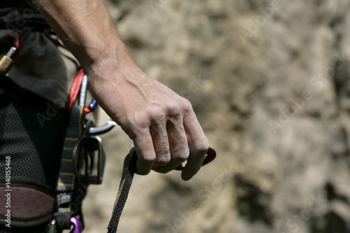 Male hand with a carabiner on a rope in front of a rocky wall, close-up, selective focus