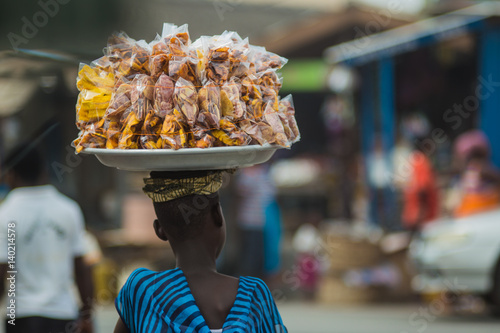 African woman carrying plantain and cassava chips on her head as she walks through a market in Cape Coast, Ghana