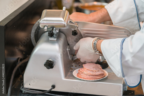 chef wearing rubber glove using ham slicer machine