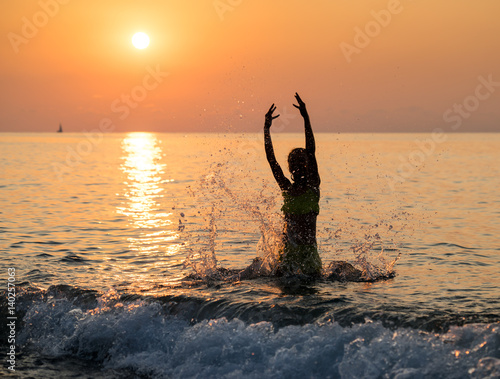 Silhouette of young girl jumping in sea