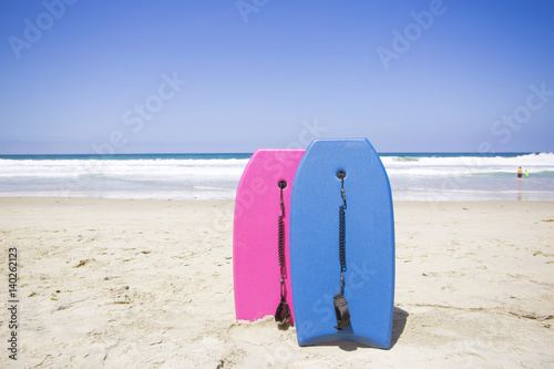 Two colorful boogie boards resting on a pristine beach. Ready to ride and have fun in the ocean on a clear summer day. Vacation time