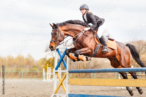 Young horseback sportsgirl jumping over obstacles on show jumping competition