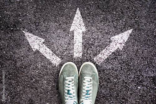 Sneakers shoes and arrows pointing in different directions on asphalt floor, life and studies choice for young people concept